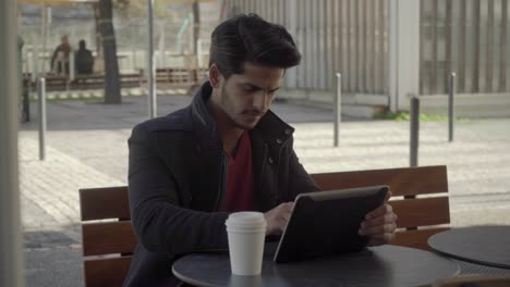 Man-drinking-from-paper-cup-and-using-digital-tablet